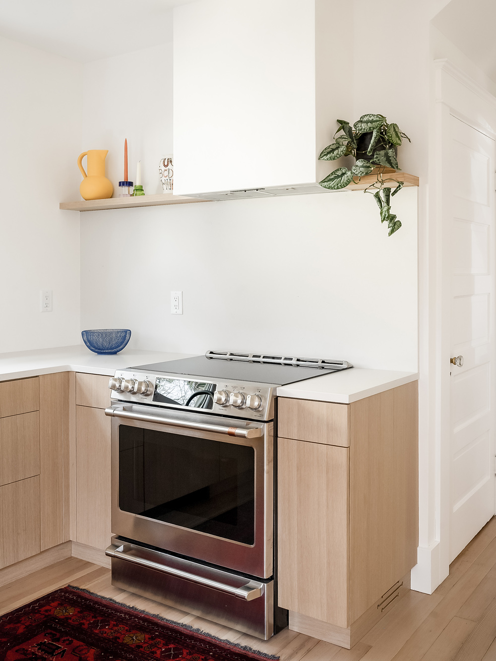 Range with white plaster backsplash and floating oak shelf above, Alameda Kitchen by Tweto Architecture