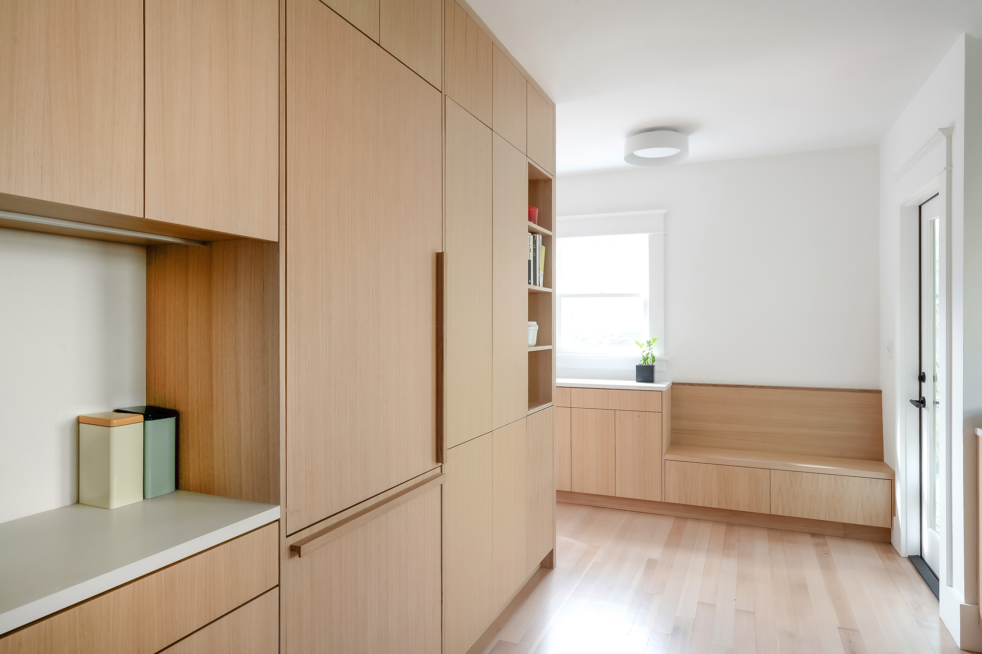 Full-height white oak cabinet wall with integrated coffee station and refrigerator, built-in bench visible beyond, Alameda Kitchen by Tweto Architecture