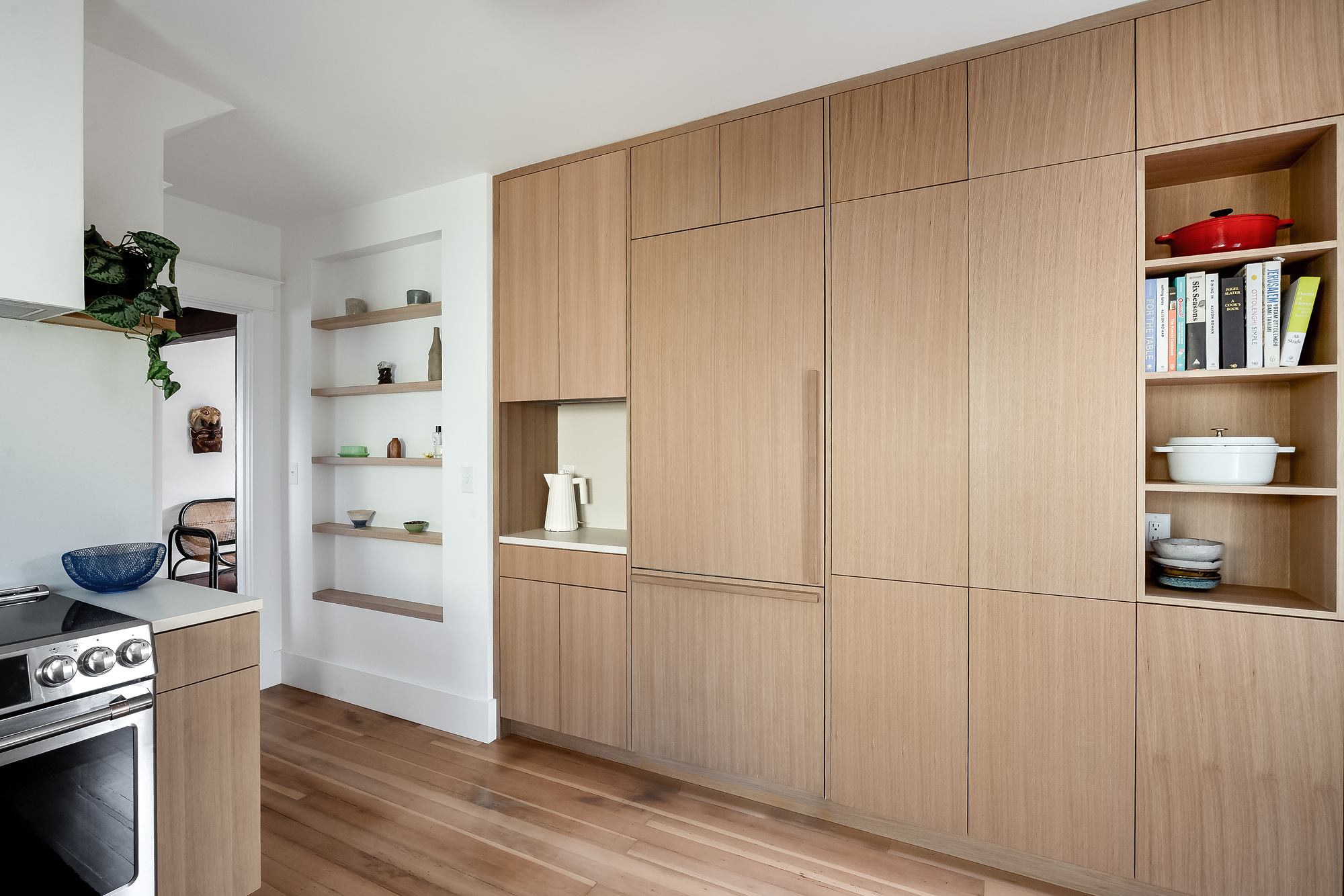 Full-height white oak storage wall with integrated refrigerator and open shelving, floating wall shelves visible in background, Alameda Kitchen by Tweto Architecture