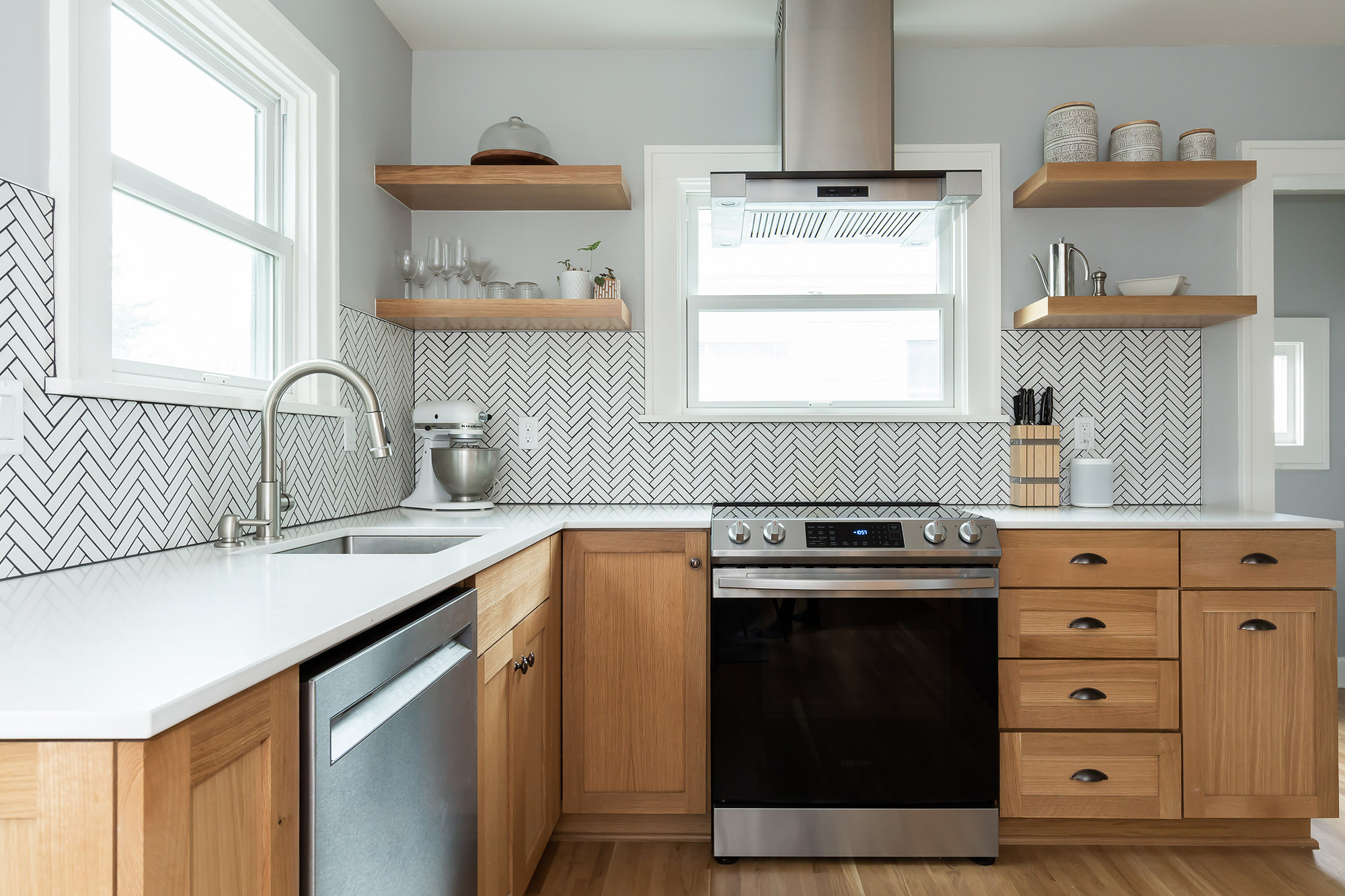 Kitchen work wall with range, sink, and herringbone tile backsplash under open oak shelves and a steel chimney hood, Arbor Lodge Kitchen remodel by Tweto Architecture, N Portland
