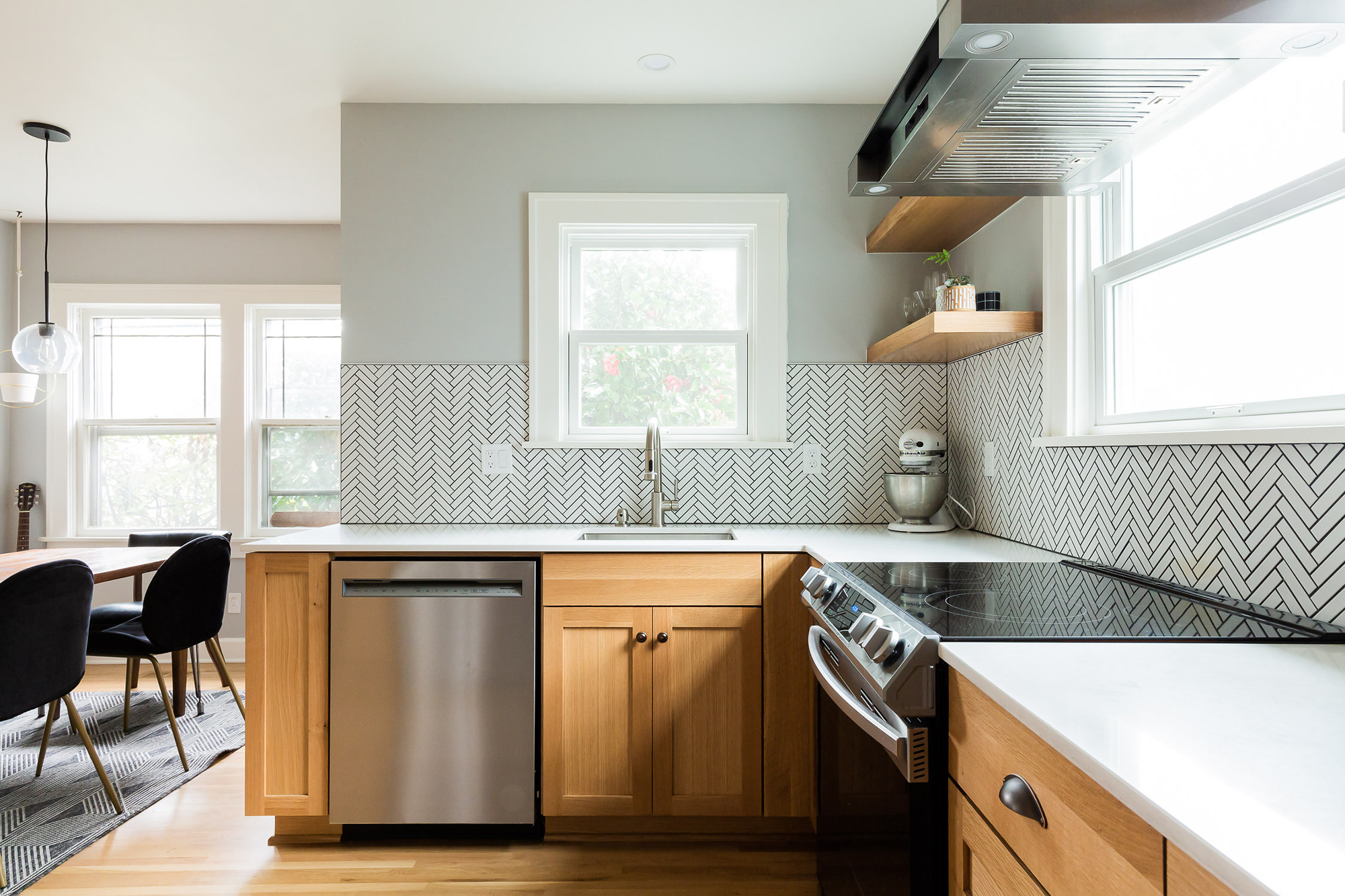 Remodeled kitchen main work wall with sink, dishwasher, range, herringbone tile backsplash, and open shelving, Arbor Lodge Kitchen by Tweto Architecture