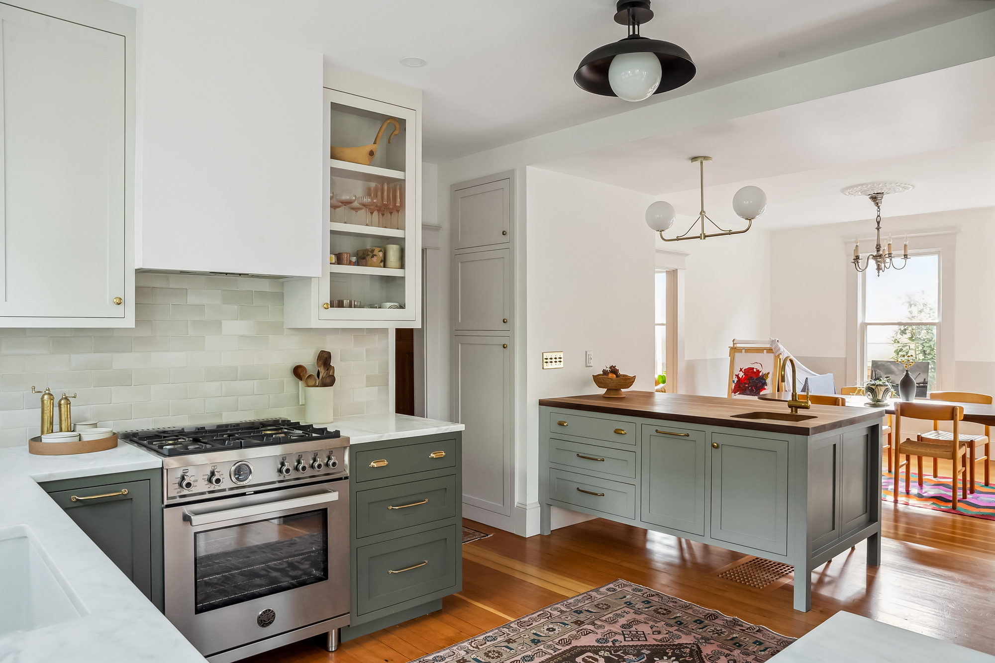 Kitchen with stainless range, green lower cabinets, and island with walnut countertop opening to the dining room beyond, Baldwin Street remodel by Tweto Architecture