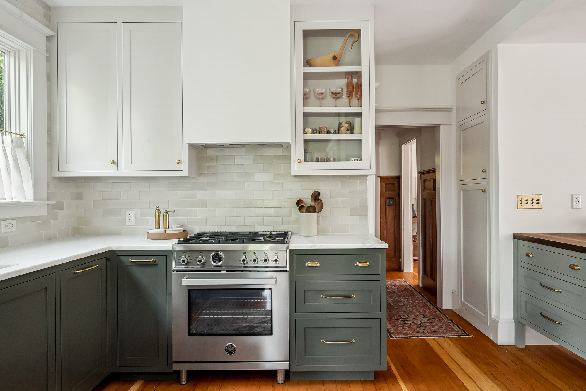 Range wall with stainless range, green lower cabinets, white upper cabinets, and handmade tile backsplash, Baldwin Street remodel by Tweto Architecture