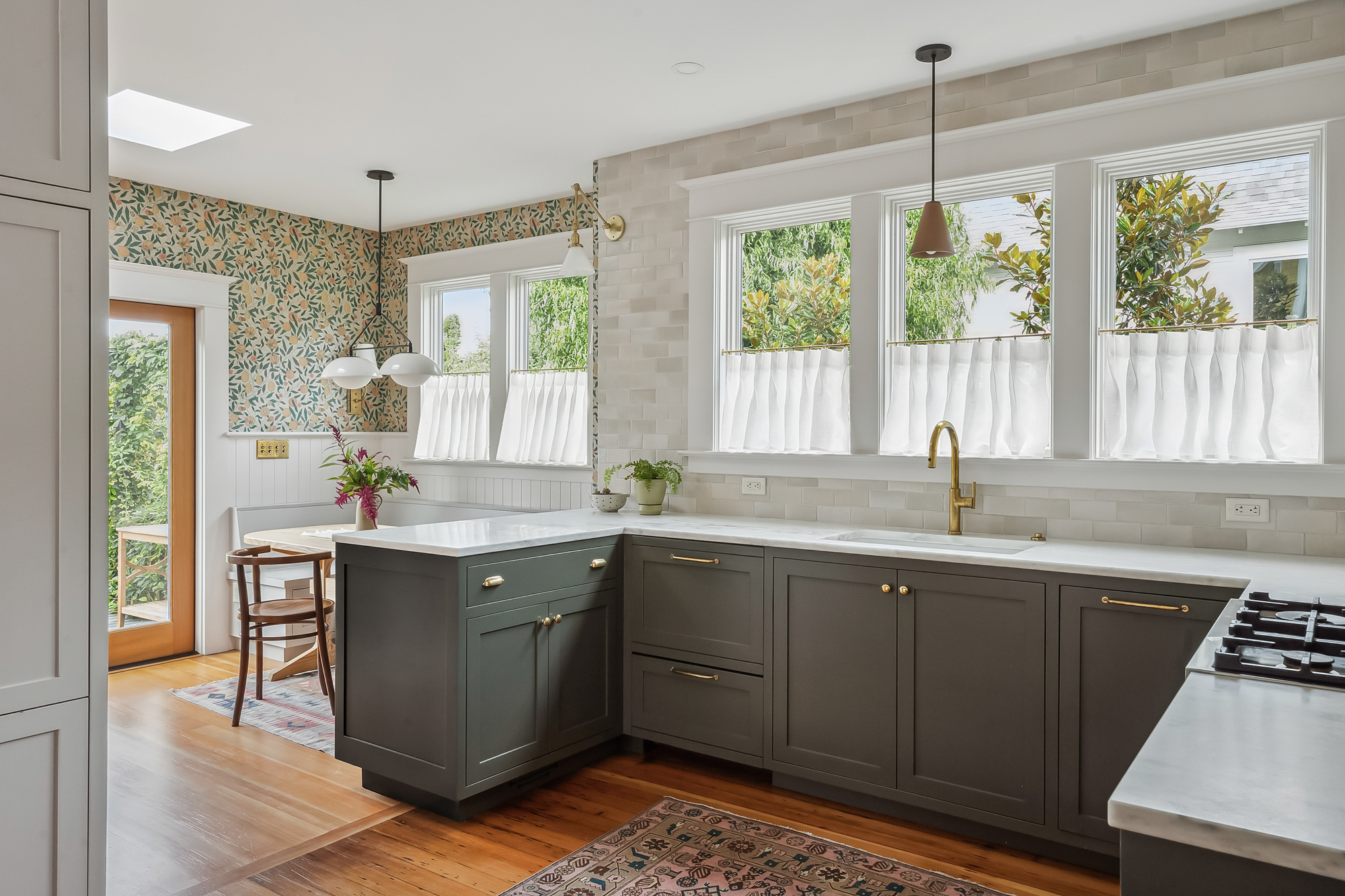 View from the breakfast nook toward the kitchen, showing the sink wall with windows, botanical wallpaper, and back door to the deck, Baldwin Street remodel by Tweto Architecture