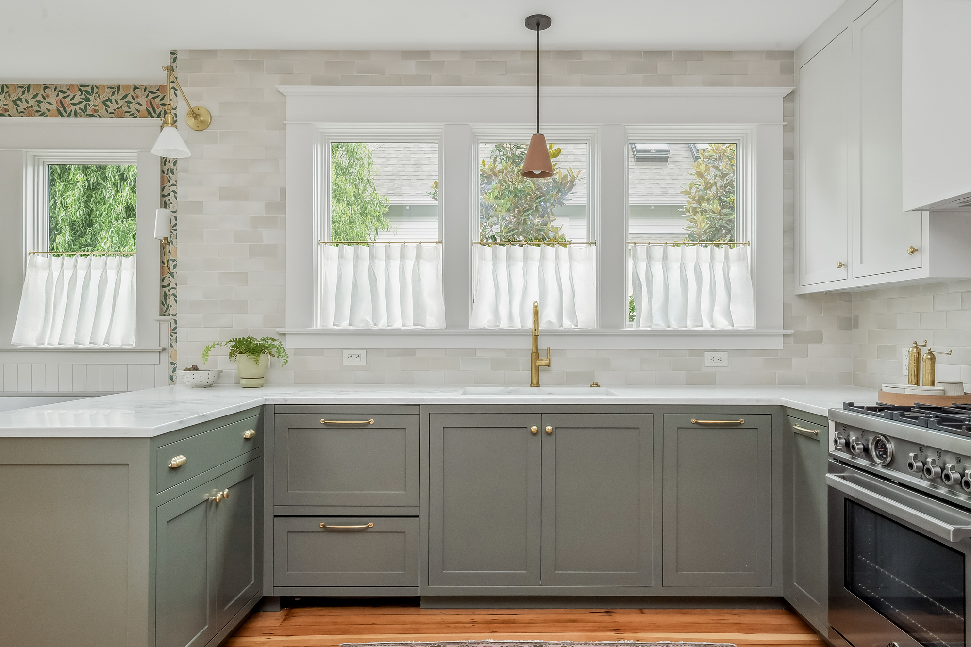 Sink wall with brass faucet, triple windows with white cafe curtains, and handmade tile backsplash, Baldwin Street remodel by Tweto Architecture