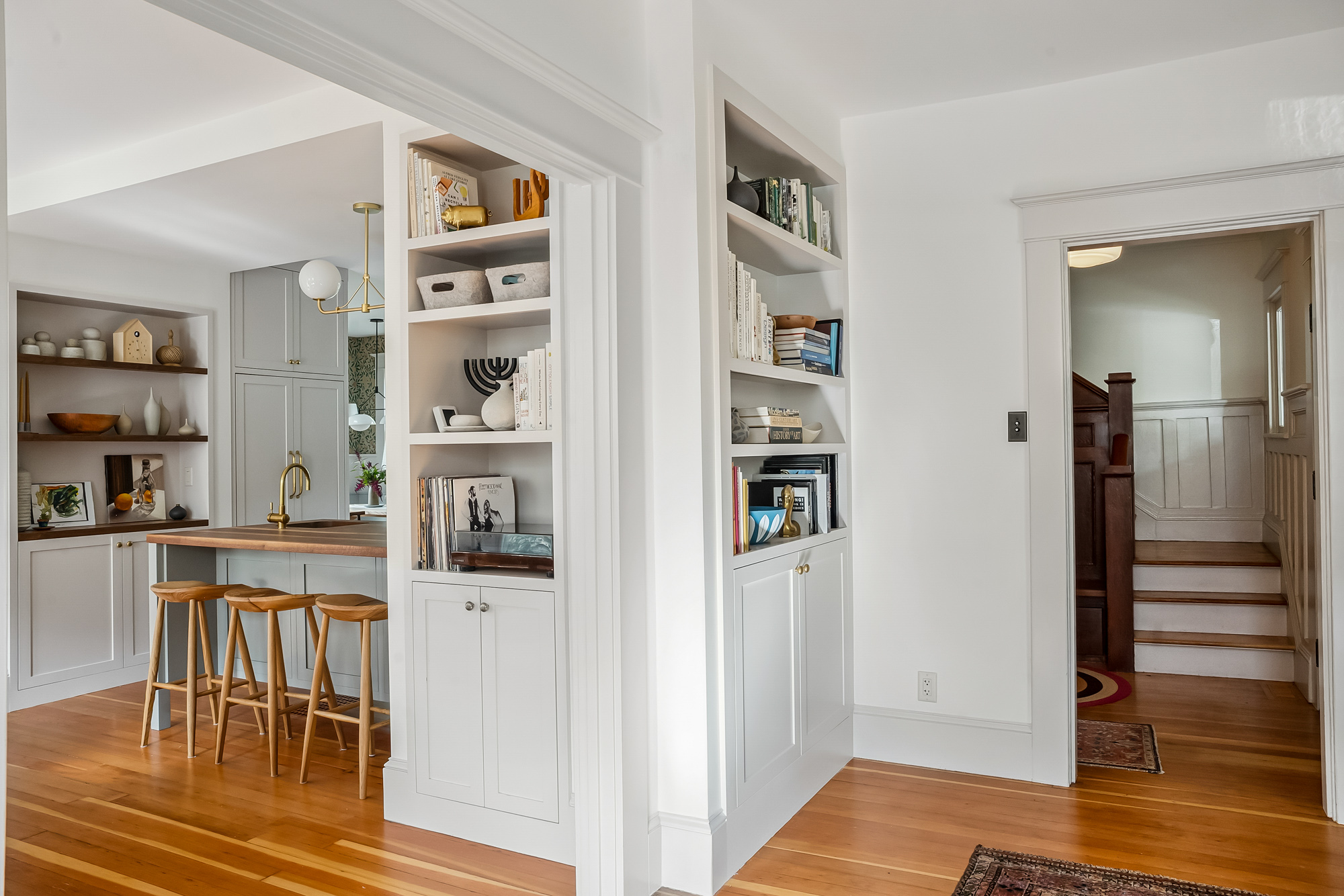 Built-in bookcases flanking a doorway to the stair hall, with the kitchen and island visible through an opening at left, Baldwin Street remodel by Tweto Architecture
