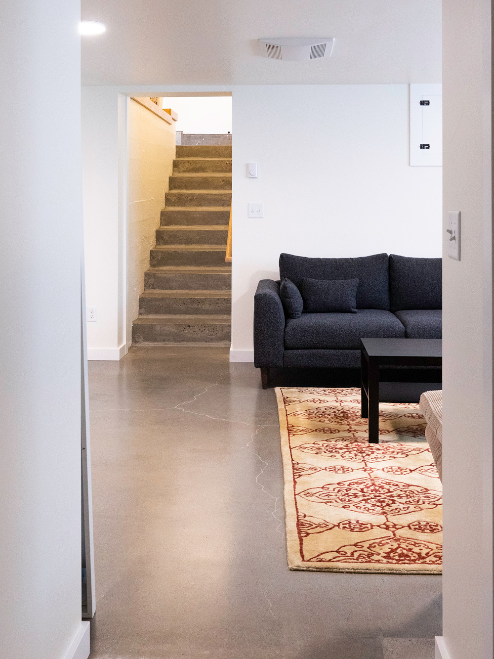 Finished basement family room with polished concrete floor and existing concrete stair visible, Brooklyn Street remodel by Tweto Architecture