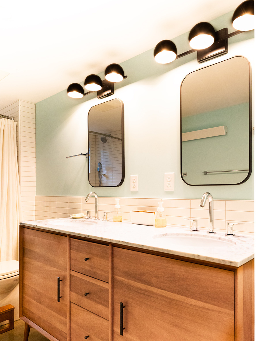 Basement bathroom double vanity with walnut cabinet, marble countertop, and rounded mirrors above, Brooklyn Street remodel by Tweto Architecture