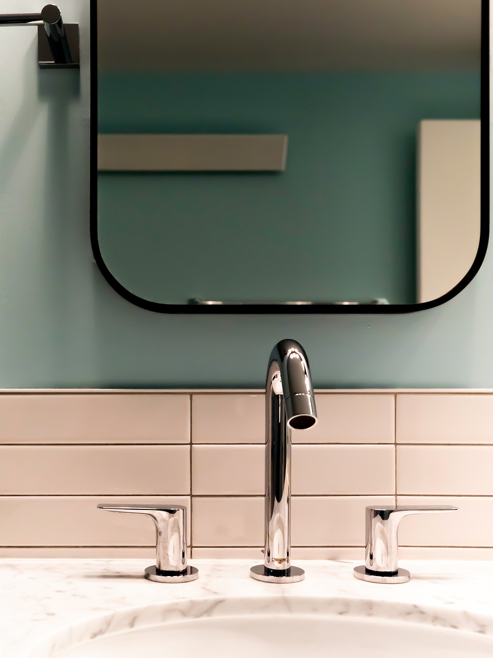 Close-up of chrome faucet and marble counter with mint green tile surround and rounded mirror above, Brooklyn Street basement bathroom by Tweto Architecture