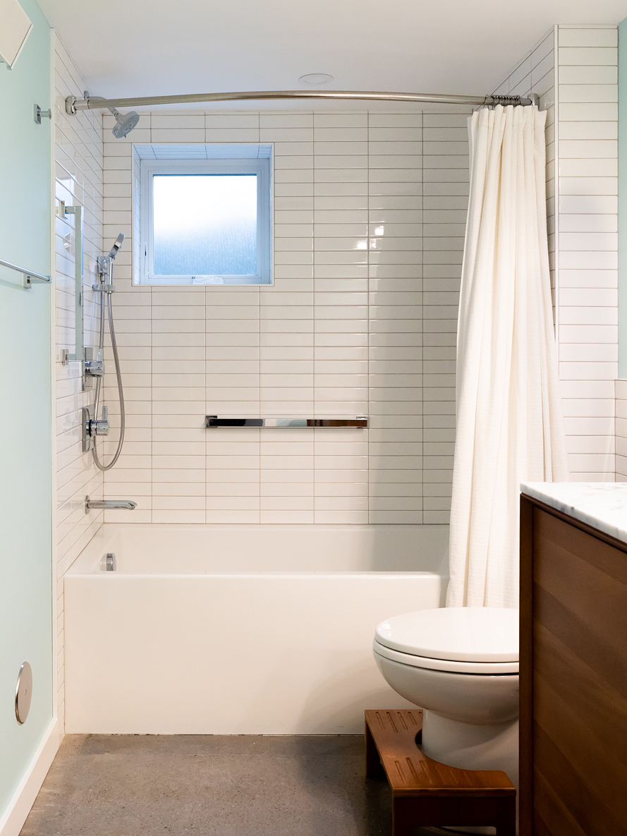 Basement bathroom tub and shower with vertical white tile, small window, and teak step stool, Brooklyn Street remodel by Tweto Architecture