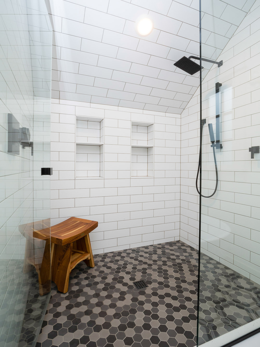 Tile shower interior with rain head, teak bench, and dark hexagon floor tile, Carolina Primary Suite addition by Tweto Architecture