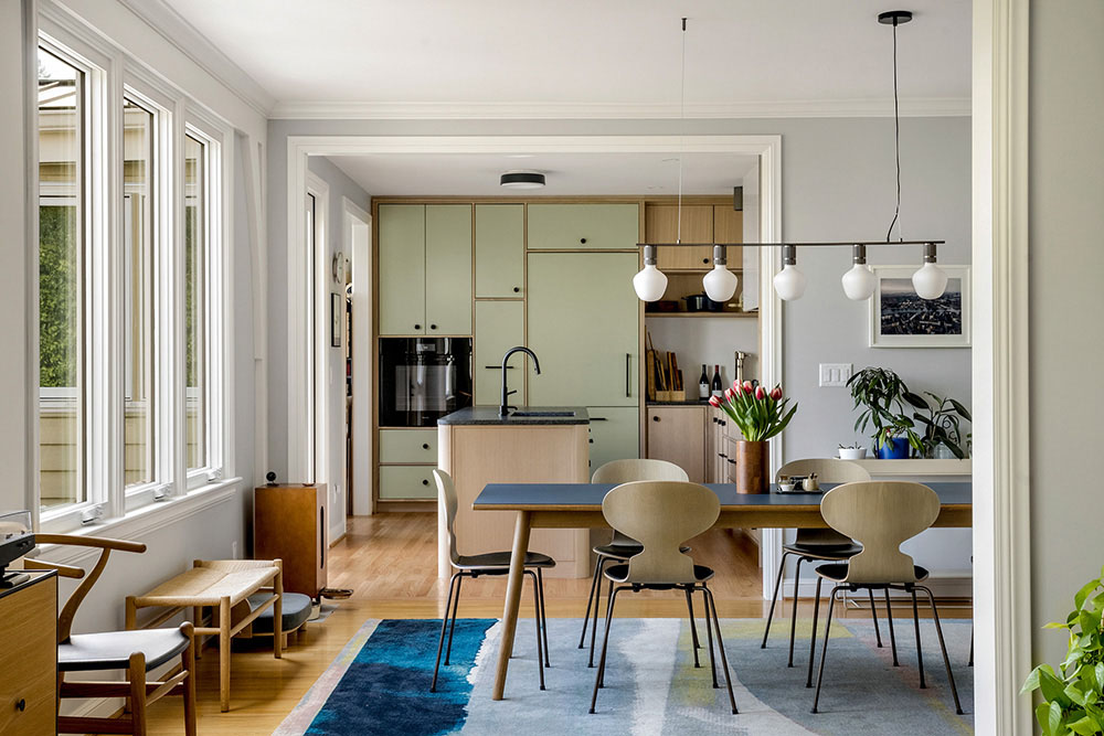 Open kitchen and dining area with sage-green cabinets, a wood island, and a blue dining table with Ant chairs, Champlain Drive Remodel by Tweto Architecture, Northwest Portland