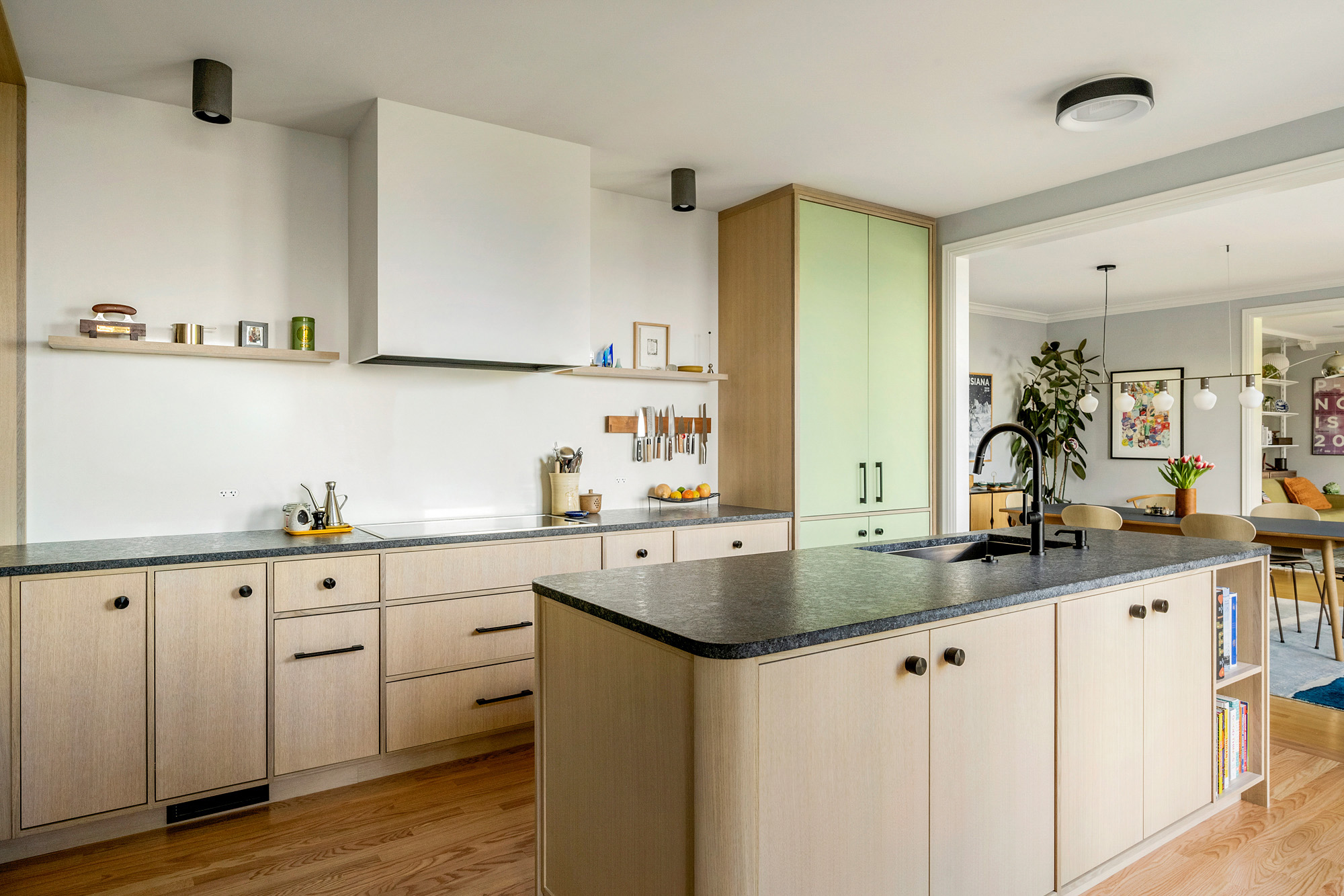 Kitchen from cooking side showing island with leathered granite, induction cooktop in counter run, and doorway to dining room visible at right, by Tweto Architecture