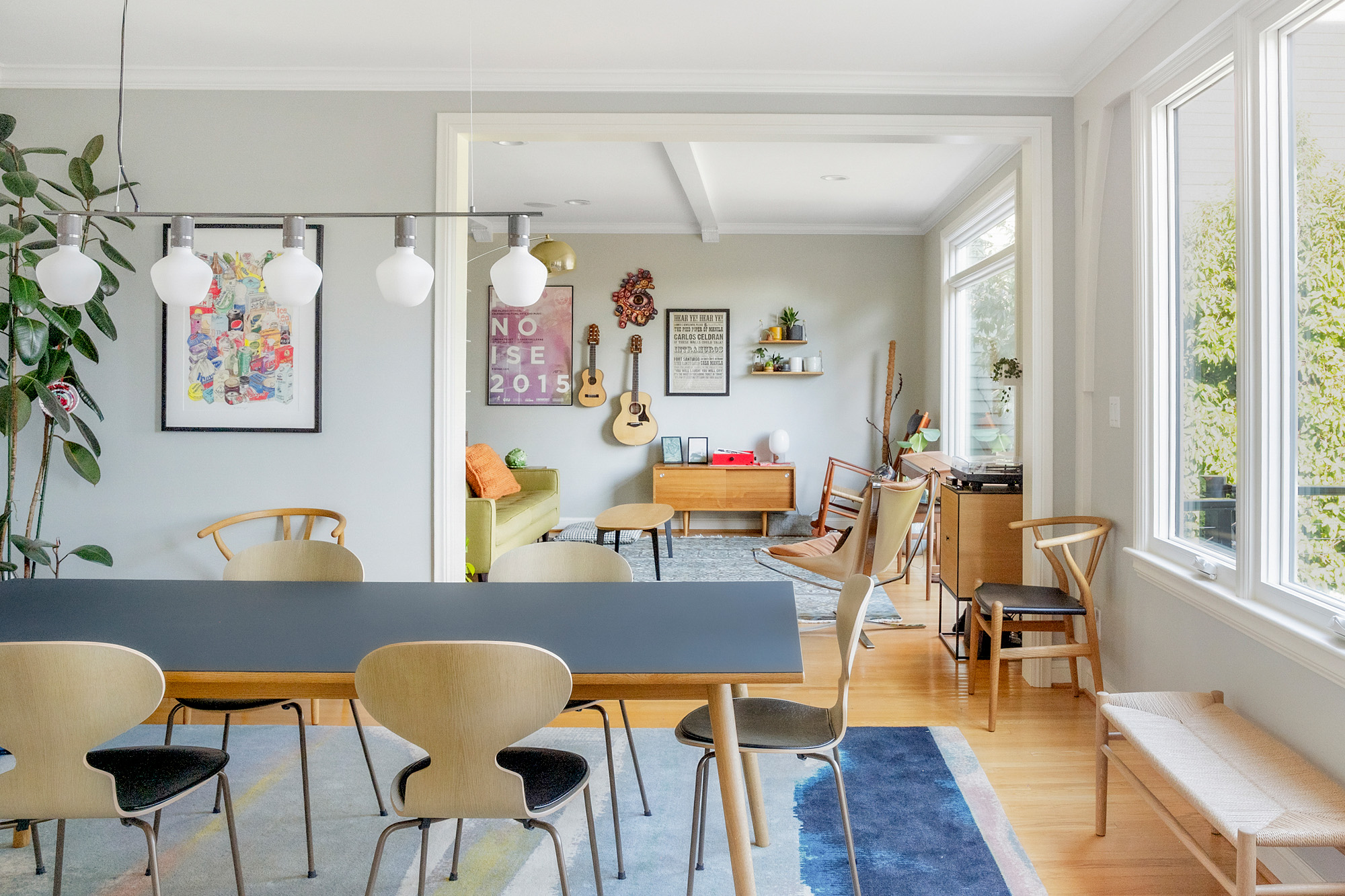 Dining room with large new windows, dining table with Ant chairs, and open view to living room with guitars on the wall beyond, by Tweto Architecture