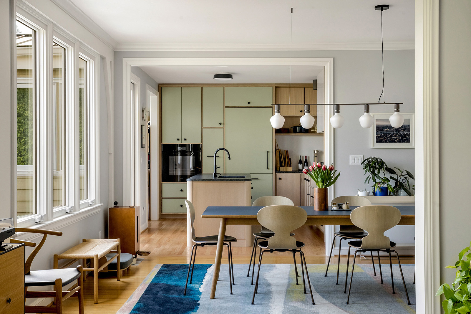 Remodeled kitchen with sage green cabinets and wood island, viewed from the dining room, by Tweto Architecture