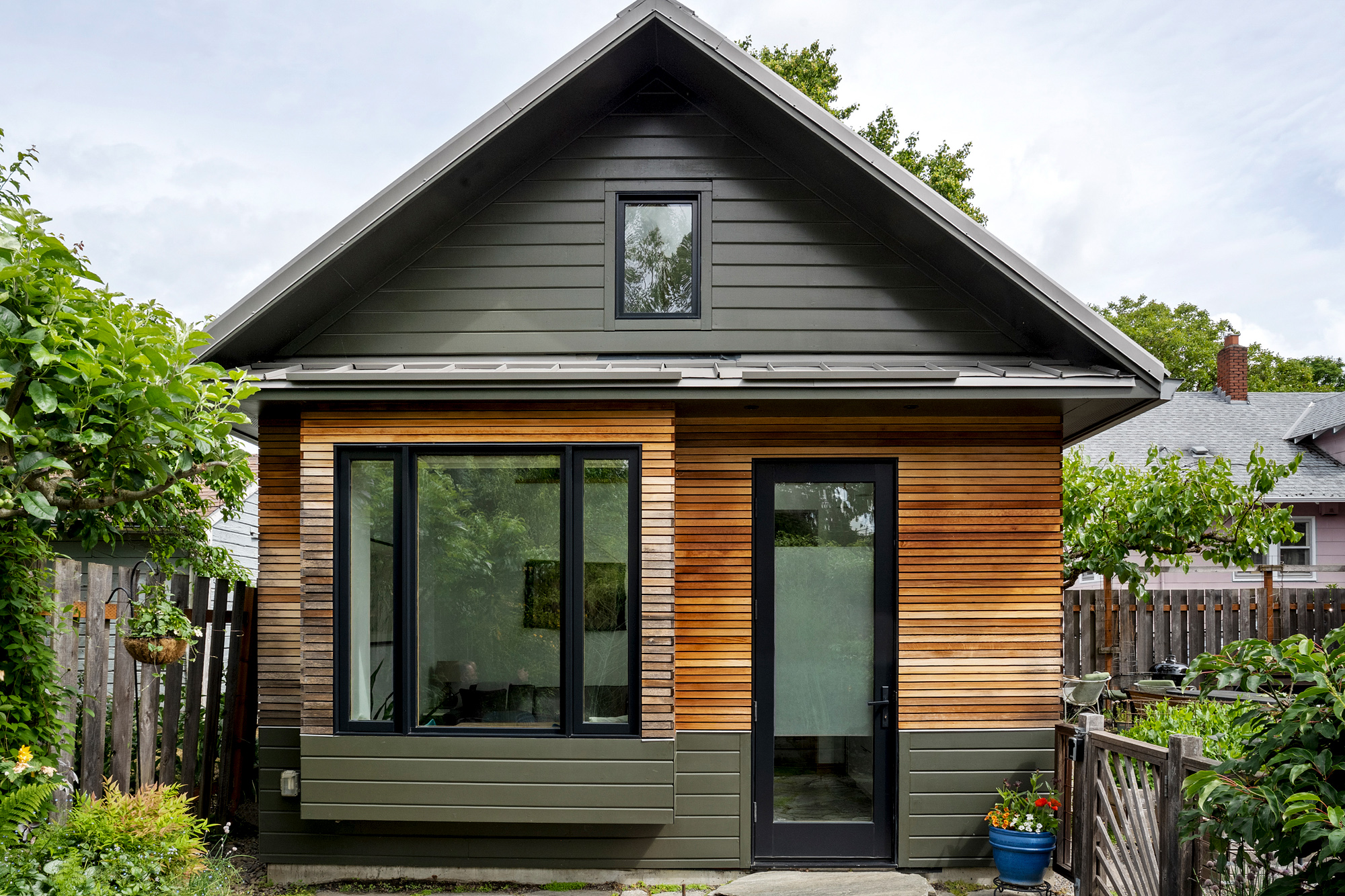 Front elevation of the Irving Park ADU with cedar lap siding, glazed French doors, and a window beneath a standing-seam metal roof, by Tweto Architecture