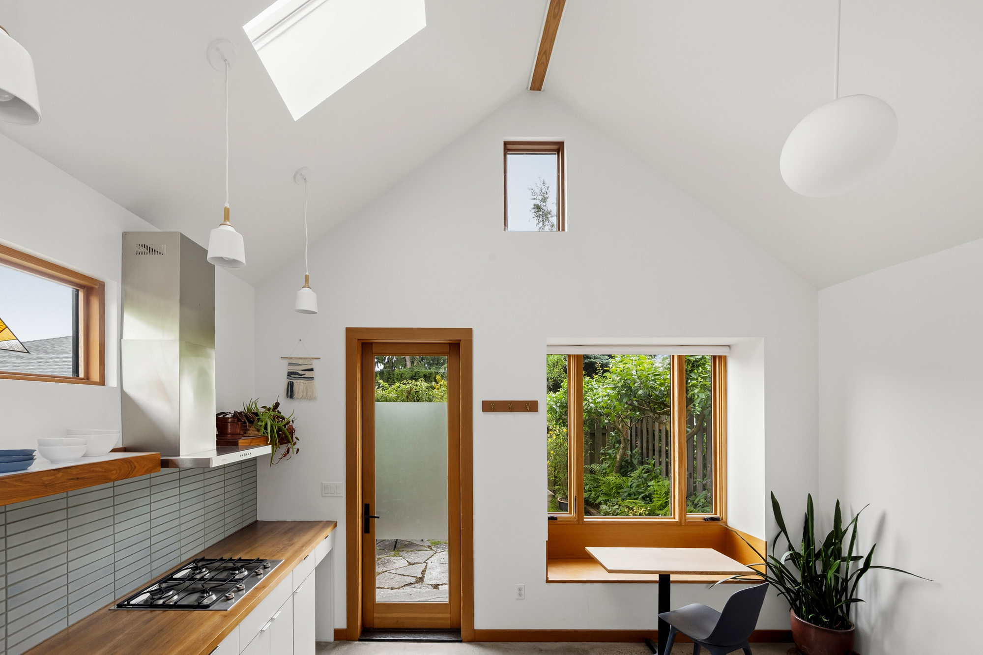 Kitchen and living area with partially vaulted ceiling, skylight, and exposed ridge beam, opening through a glazed door and bay window to the garden, Irving Park ADU by Tweto Architecture