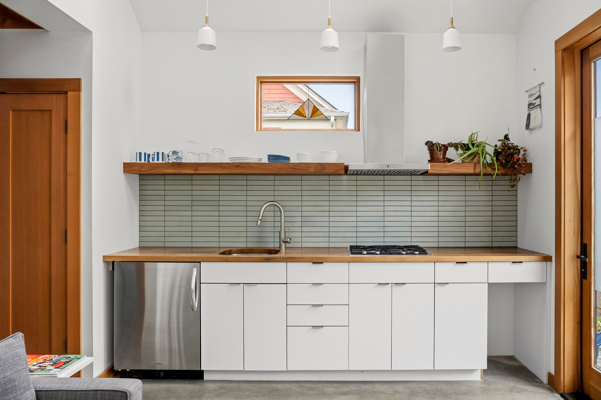 Kitchen with white cabinets, butcher block counters, sage green tile backsplash, gas range, and open wood shelving, Irving Park ADU by Tweto Architecture