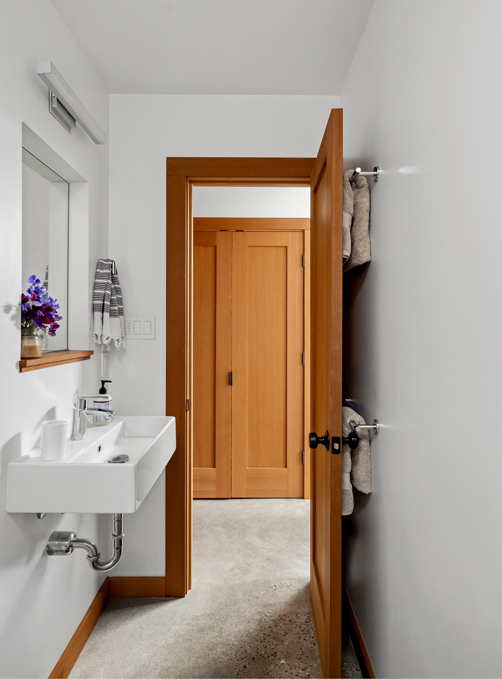 Bathroom vanity with a wall-hung sink and mirror, looking through to the closet with built-in Douglas Fir doors, Irving Park ADU by Tweto Architecture