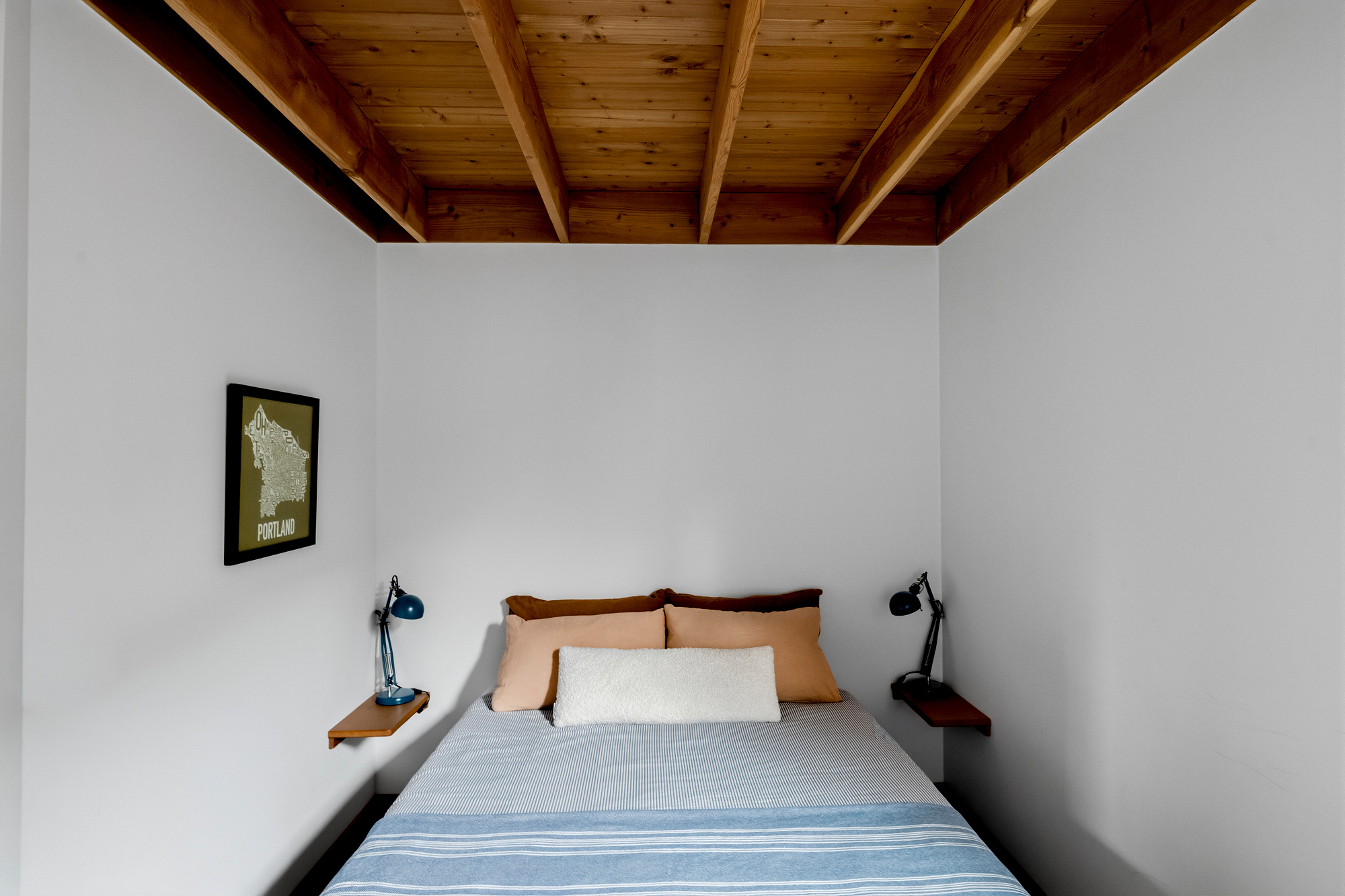 Bedroom with exposed wood ceiling, bed with blue and cream bedding, and built-in nightstands with reading lamps, Irving Park ADU by Tweto Architecture