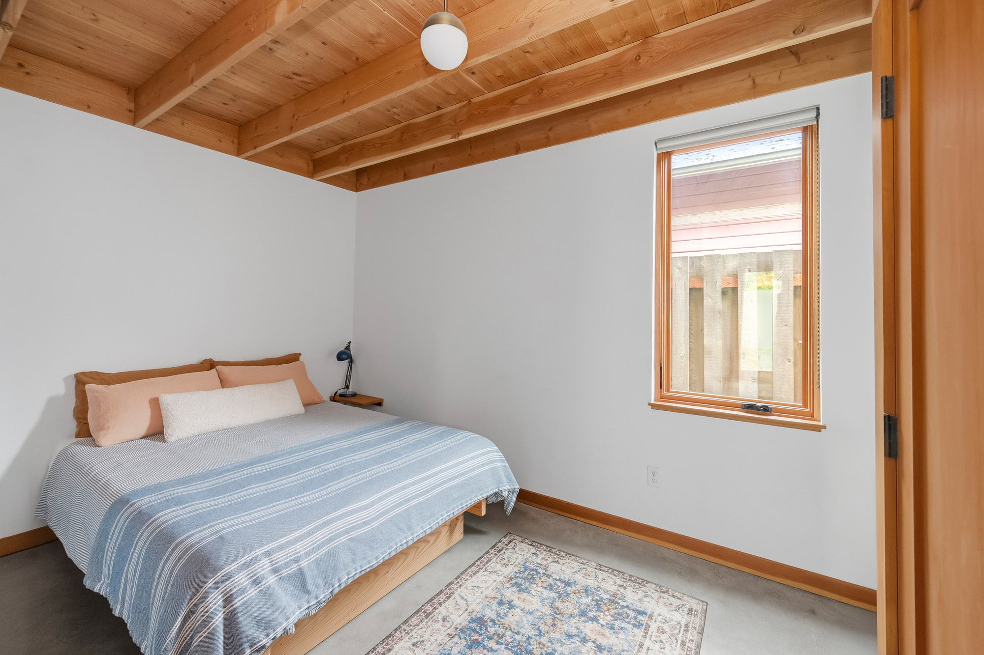 Bedroom with exposed wood ceiling and a window looking out over the side yard, Irving Park ADU by Tweto Architecture