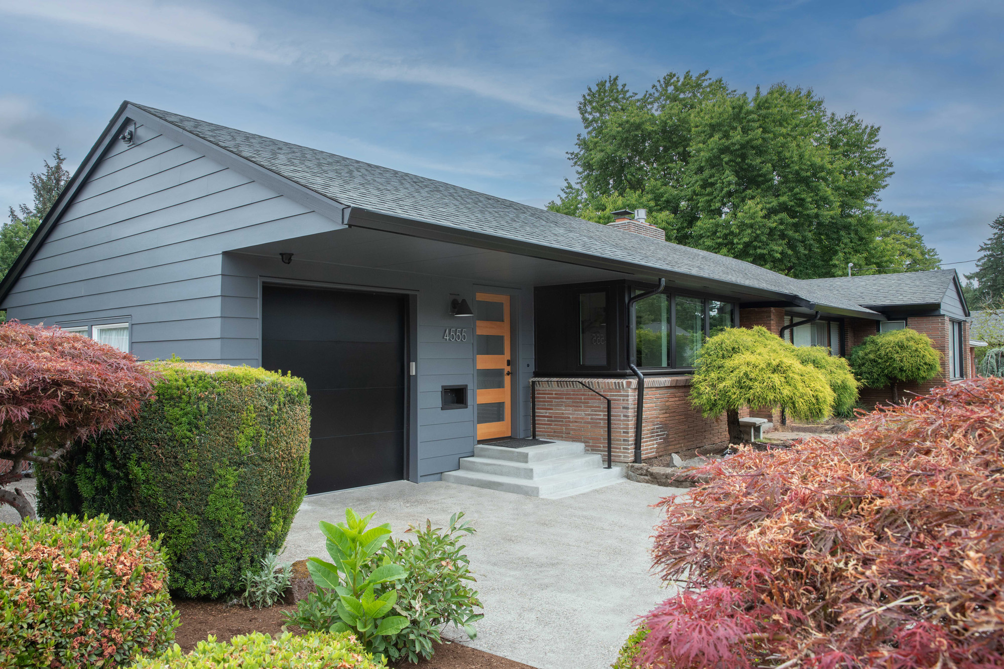 Remodeled mid-century ranch exterior with new gray siding, wood front door with glass panels, and Japanese maple plantings, SE Portland by Tweto Architecture