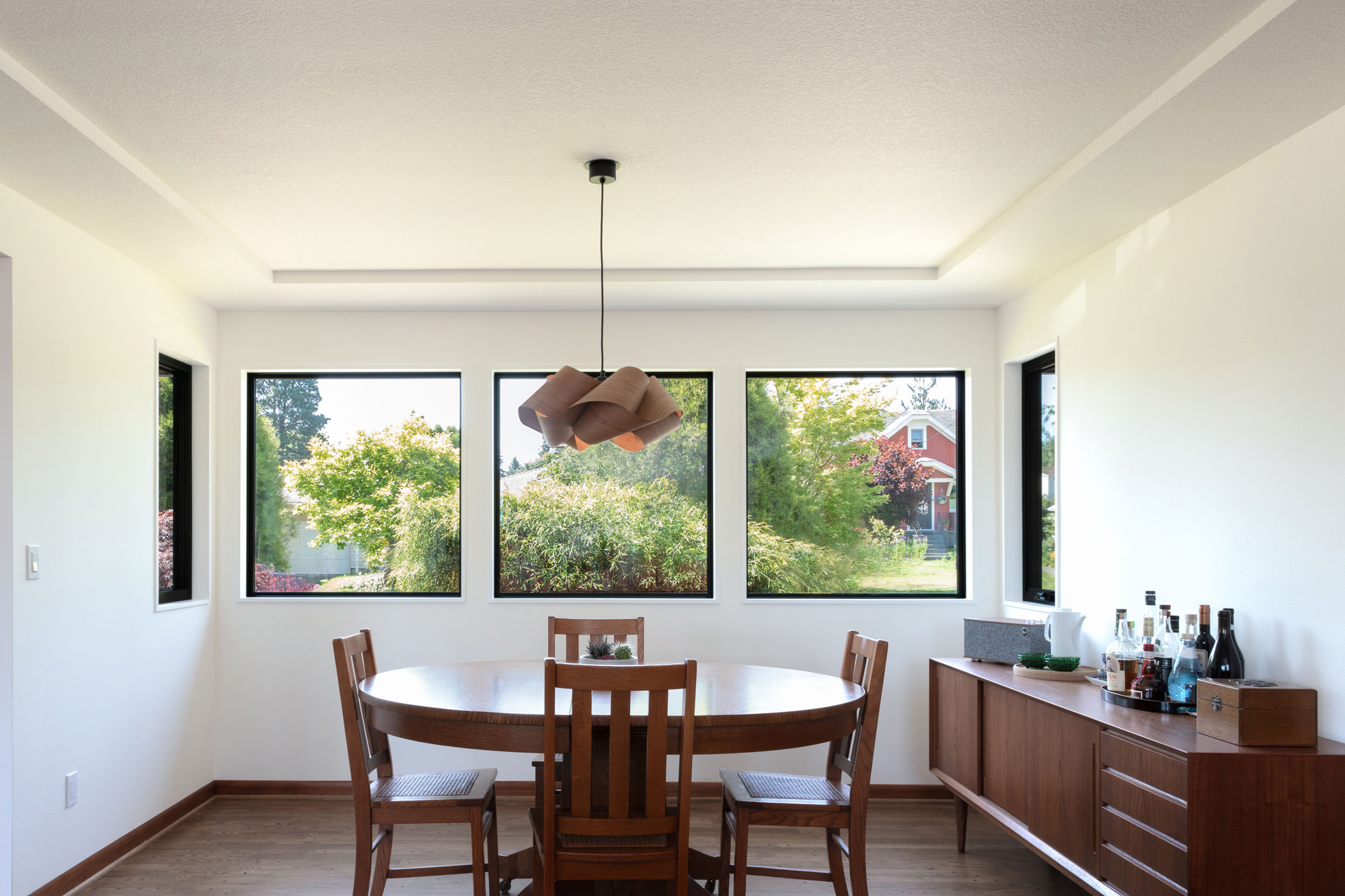 Dining room with three large black-framed windows overlooking the garden, wood pendant light above a round table, Kelly Street remodel by Tweto Architecture