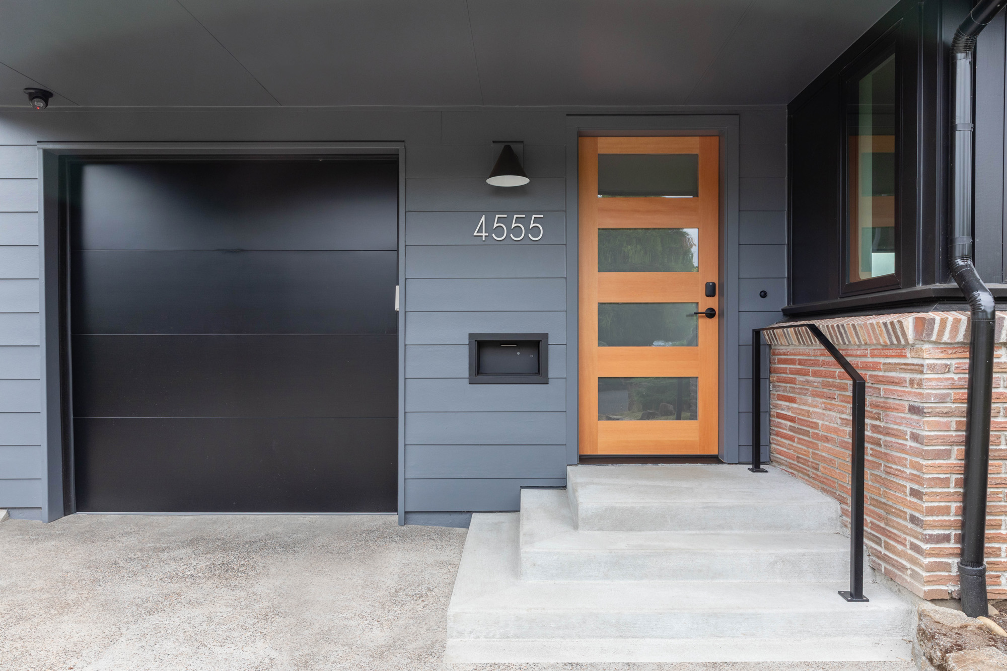 Front entry with new wood door with four glass panels, house number 4555, black garage door to the left, and brick steps with metal railing, Kelly Street remodel by Tweto Architecture