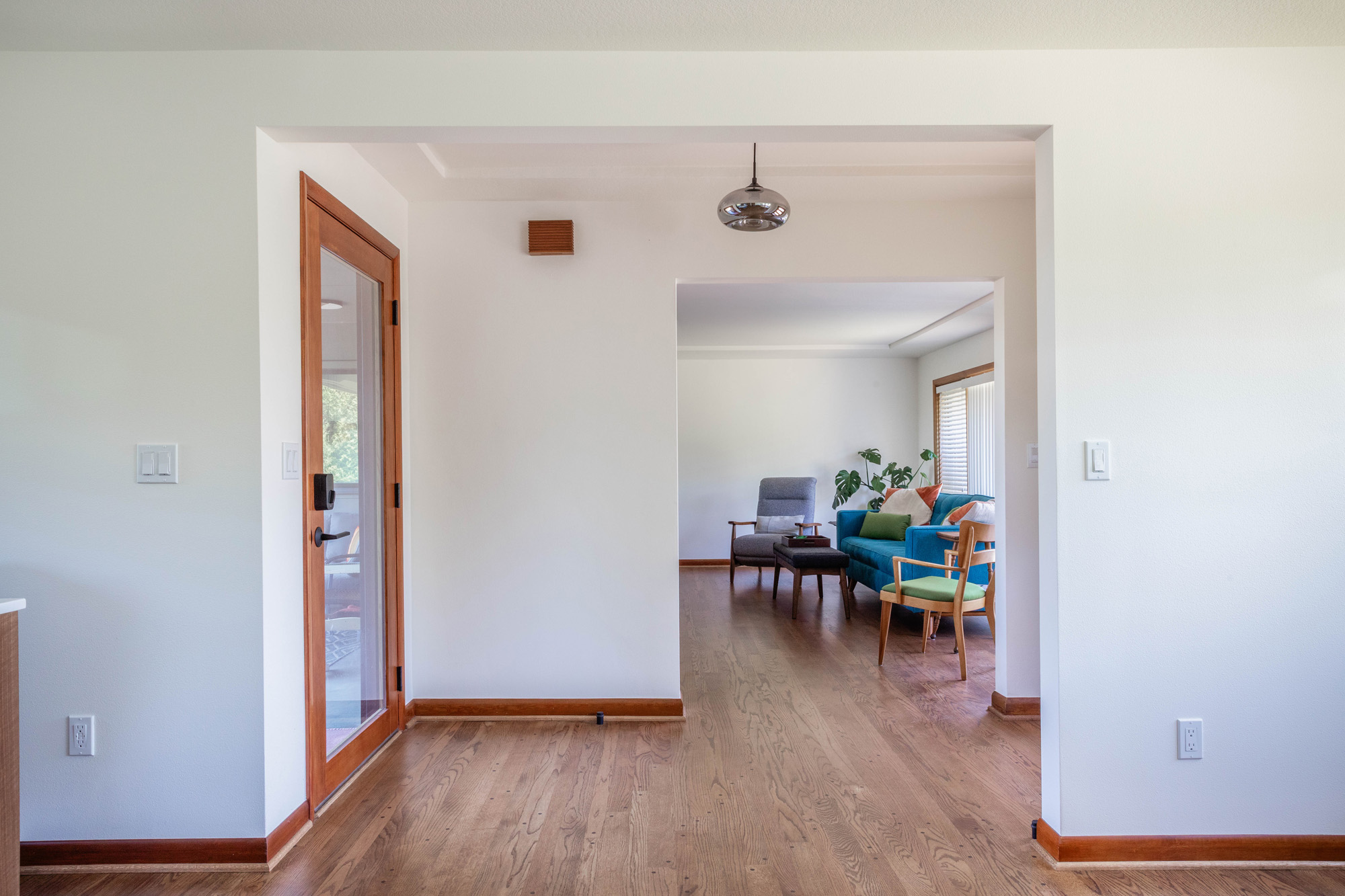 Stair hall looking through an open archway toward the living room with mid-century furniture and plants, Kelly Street remodel by Tweto Architecture