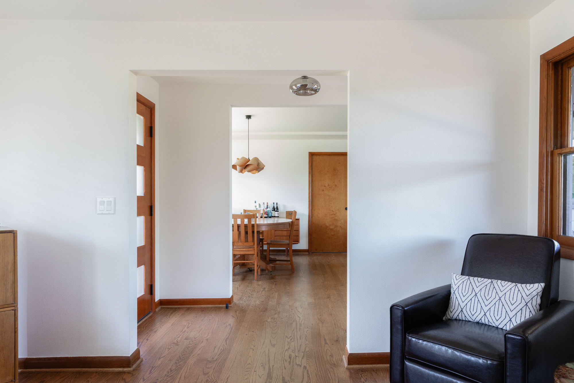 Living room looking through an opening into the dining room, original wood trim doors and new glazed door to the stair addition visible, Kelly Street remodel by Tweto Architecture