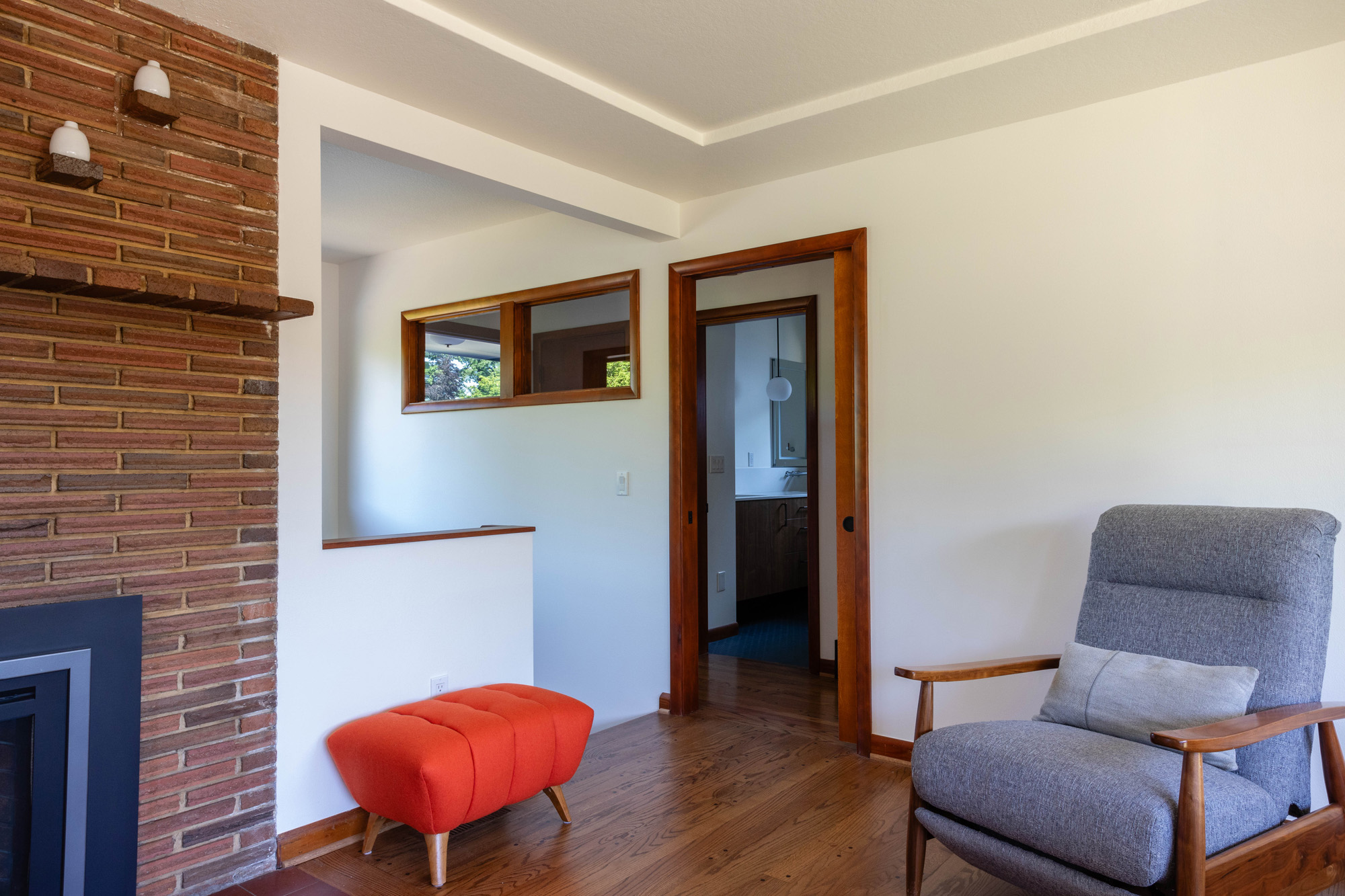 Living room with original brick fireplace, opening to the new stair addition beyond, and original wood door trim, Kelly Street remodel by Tweto Architecture