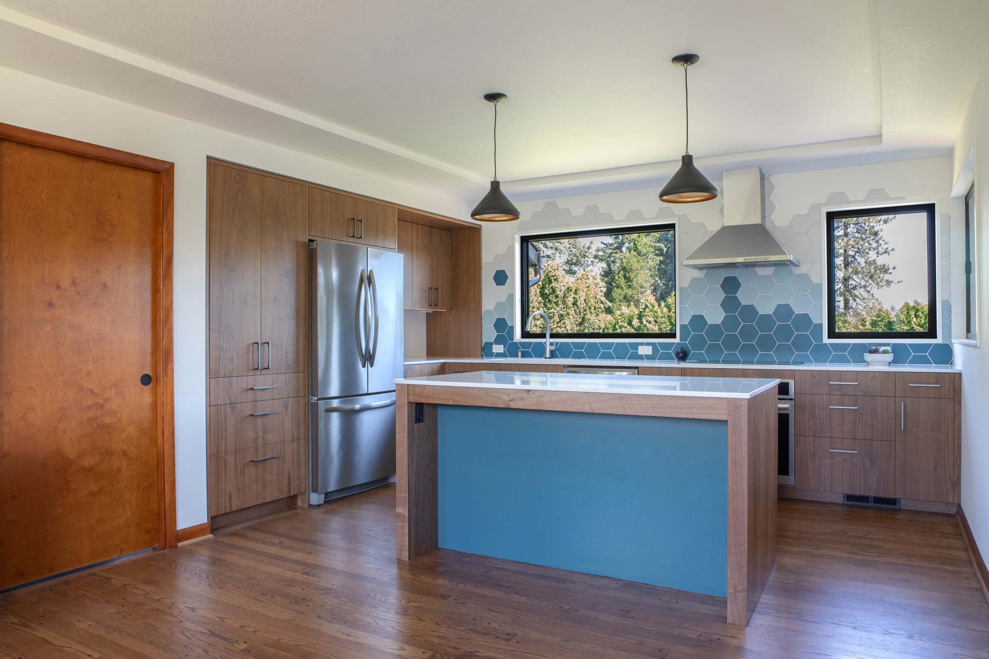 Remodeled kitchen with walnut island, blue hexagonal tile backsplash, two large backyard windows, and black pendant lights, Kelly Street remodel by Tweto Architecture