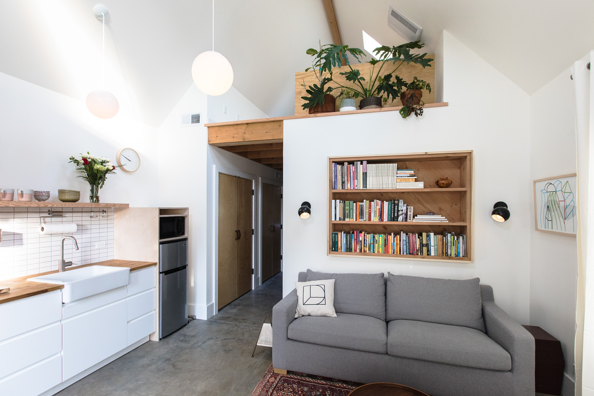 Open great room looking toward the bedroom hall, sofa and built-in wood bookcase below the loft, kitchen along the left wall, Mason Street ADU by Tweto Architecture
