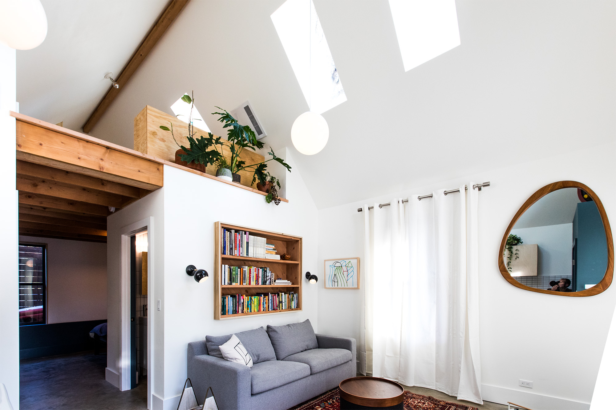Living room looking toward the south-facing front windows, vaulted ceiling with skylights and loft beam above, Mason Street ADU by Tweto Architecture