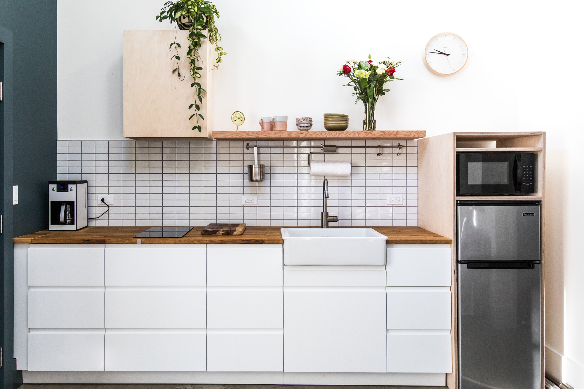 Kitchen wall with white flat-front cabinets, butcher block countertop, farmhouse sink, and white square tile backsplash, Mason Street ADU by Tweto Architecture