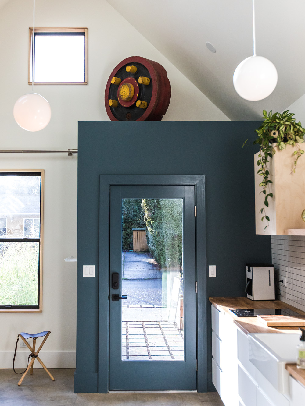 Interior view toward the glazed front door set in a deep teal-painted surround, vaulted ceiling and loft above, kitchen to the right, Mason Street ADU by Tweto Architecture