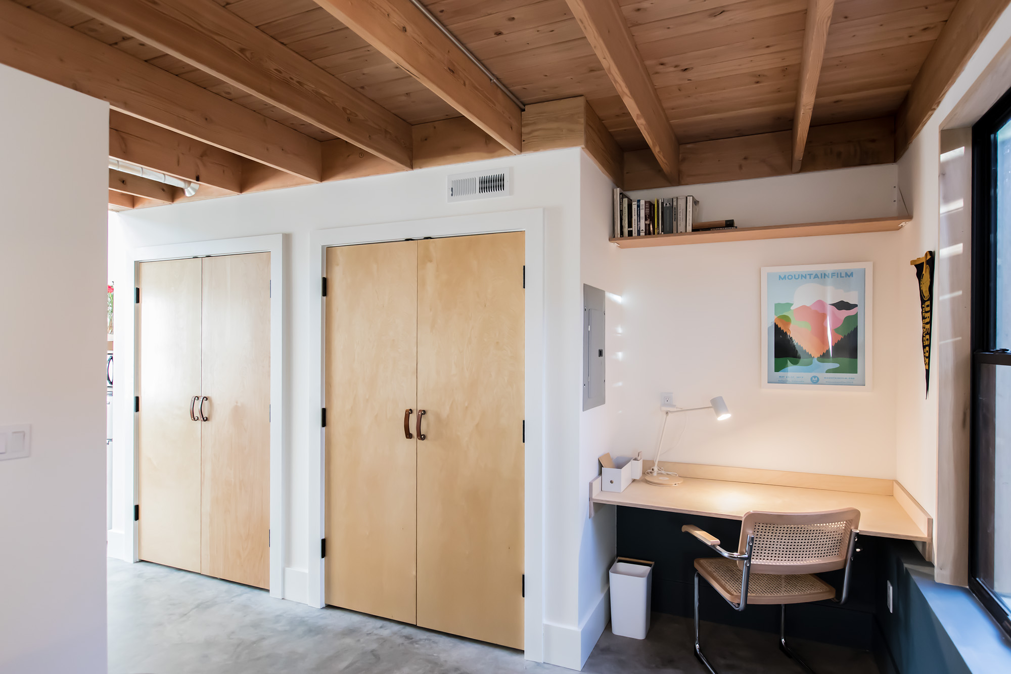 Loft level showing two plywood-door closets and a built-in desk nook with exposed fir ceiling, Mason Street ADU by Tweto Architecture