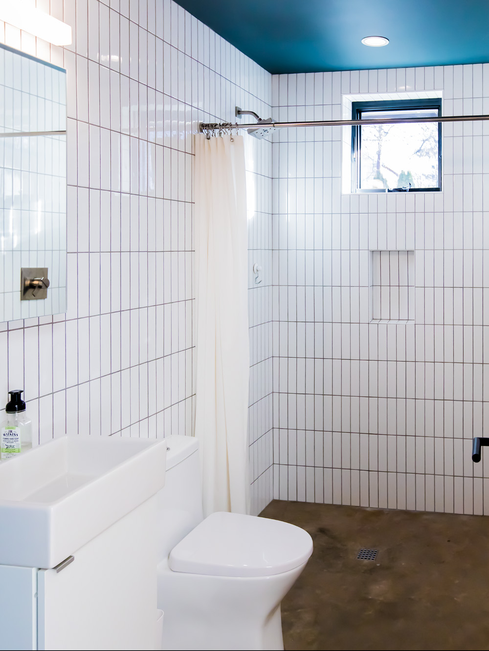 Bathroom with full white square tile walls, curbless shower with curtain rod, and teal painted ceiling, Mason Street ADU by Tweto Architecture