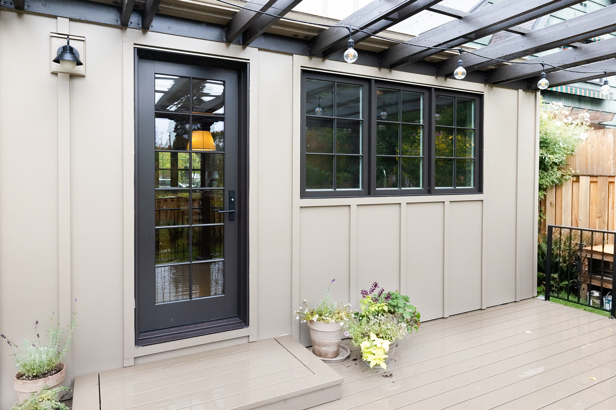 Rebuilt rear addition from backyard deck showing glass back door and casement windows with board and batten siding under pergola, Mt. Tabor Tudor remodel by Tweto Architecture