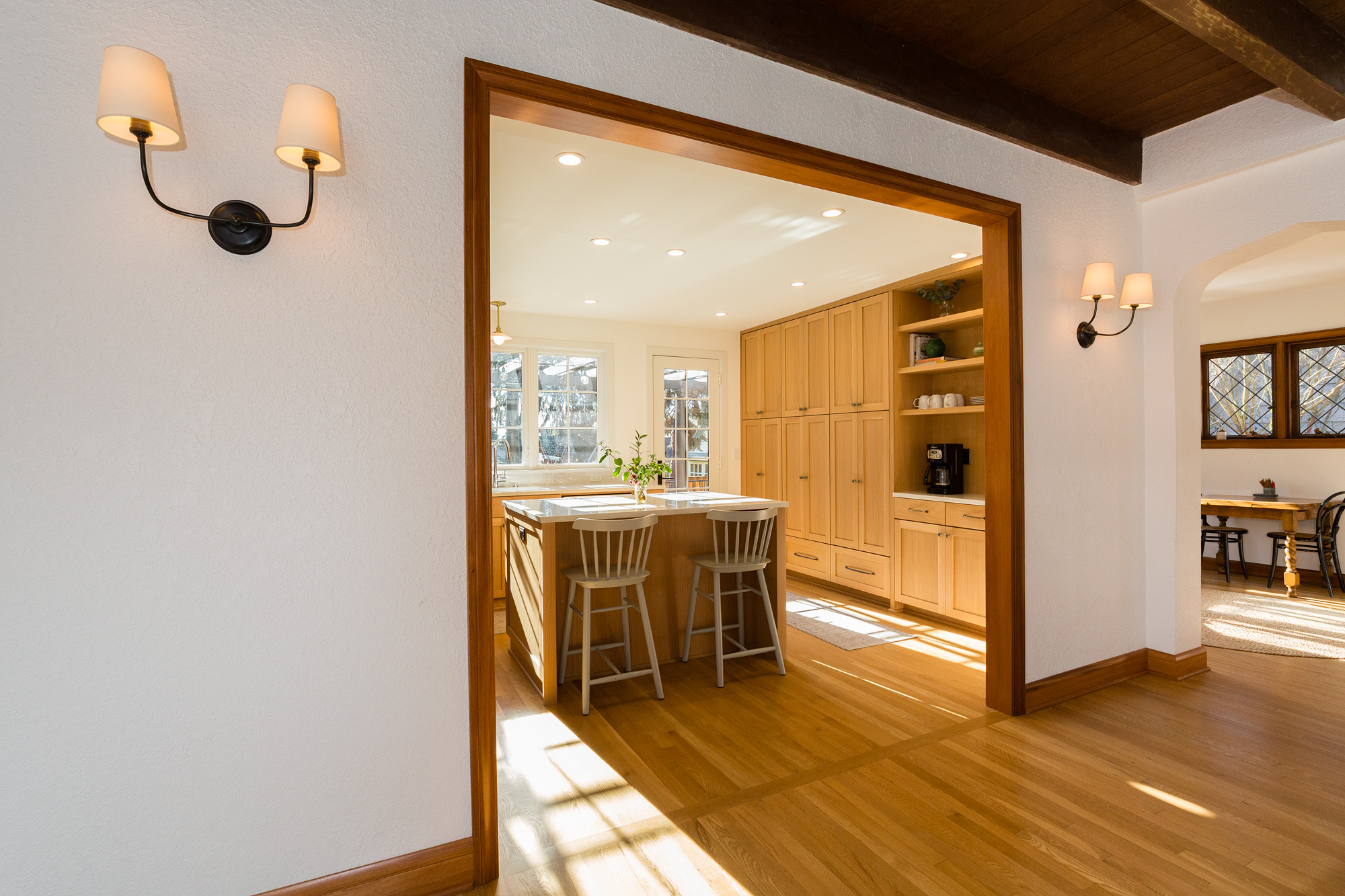 View from dining room into new kitchen through wide opening, original Tudor beamed ceiling and arched doorway visible, Mt. Tabor Tudor remodel by Tweto Architecture