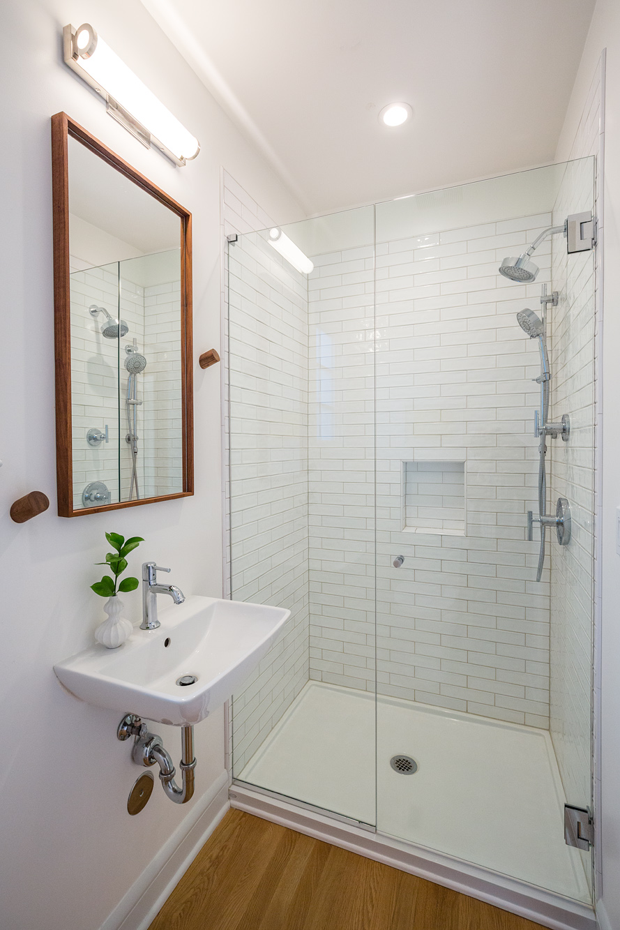 New bathroom with wall-hung sink and walk-in shower with glass door and subway tile, Mt. Tabor Tudor remodel by Tweto Architecture