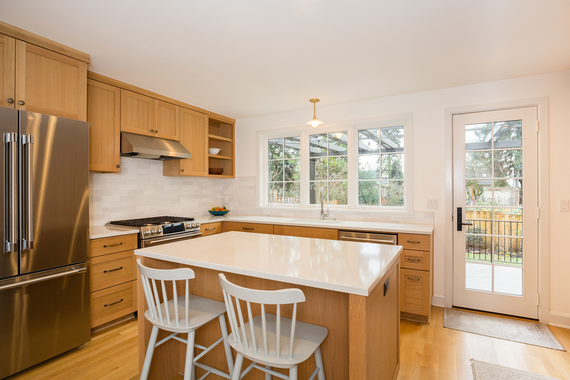 Remodeled kitchen with island, stools, three casement windows and glass back door to the backyard, Mt. Tabor Tudor remodel by Tweto Architecture