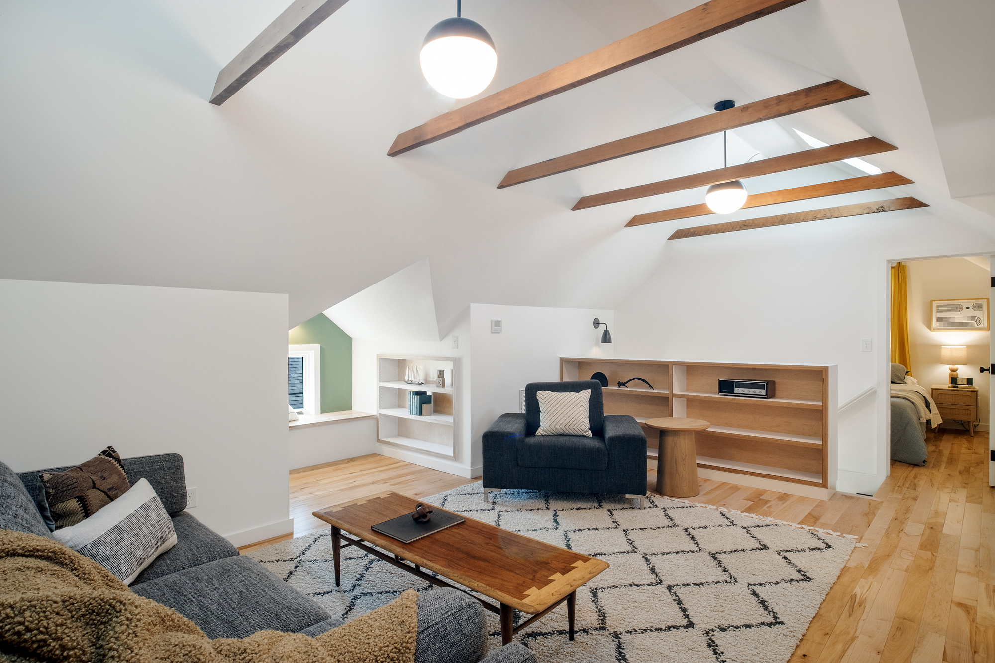 Attic living space with vaulted ceiling, two pendant lights, and built-in shelving beside the dormer niche, NE 9th Remodel by Tweto Architecture