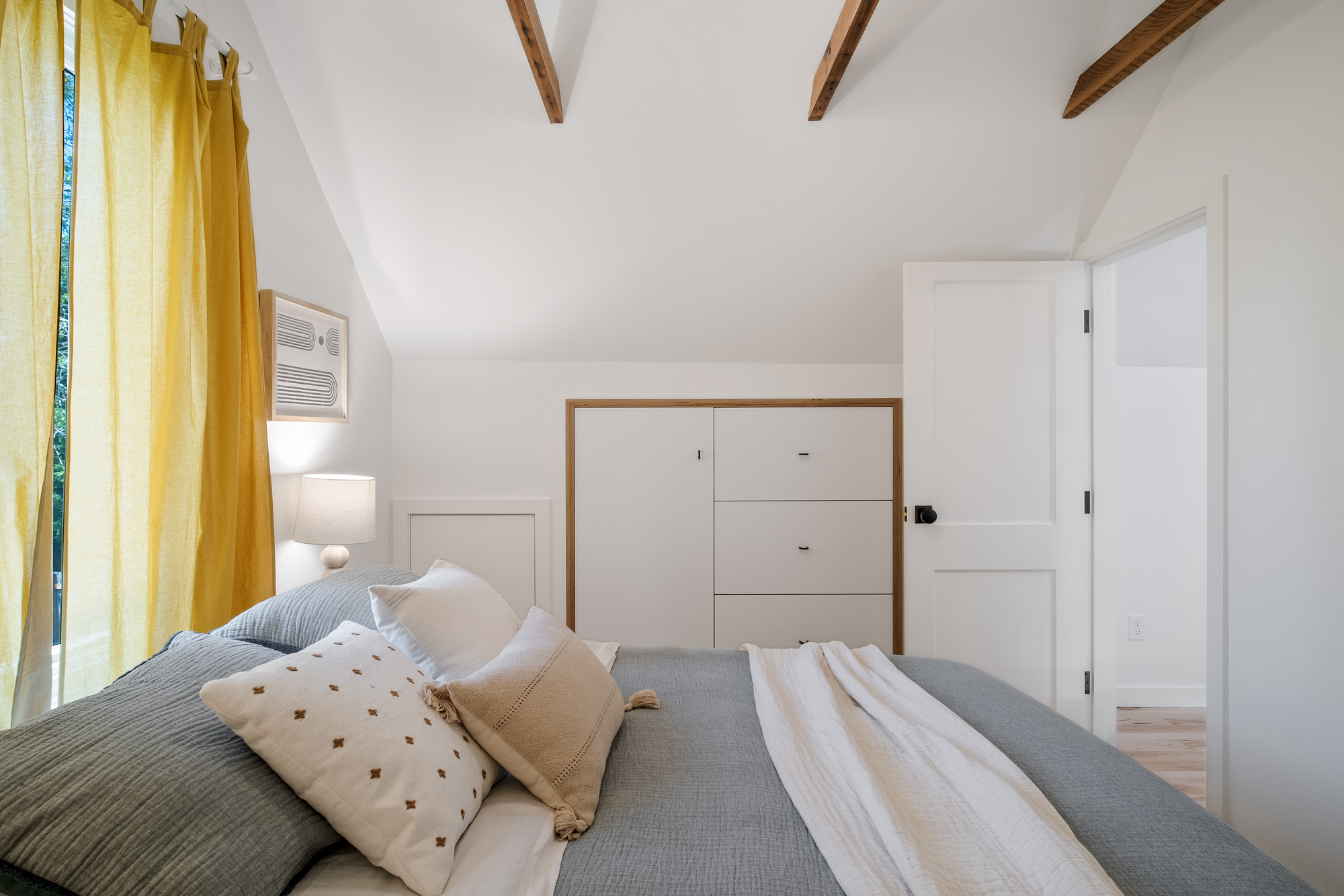 Attic bedroom showing built-in wardrobe cabinet and yellow curtains, NE 9th Remodel by Tweto Architecture
