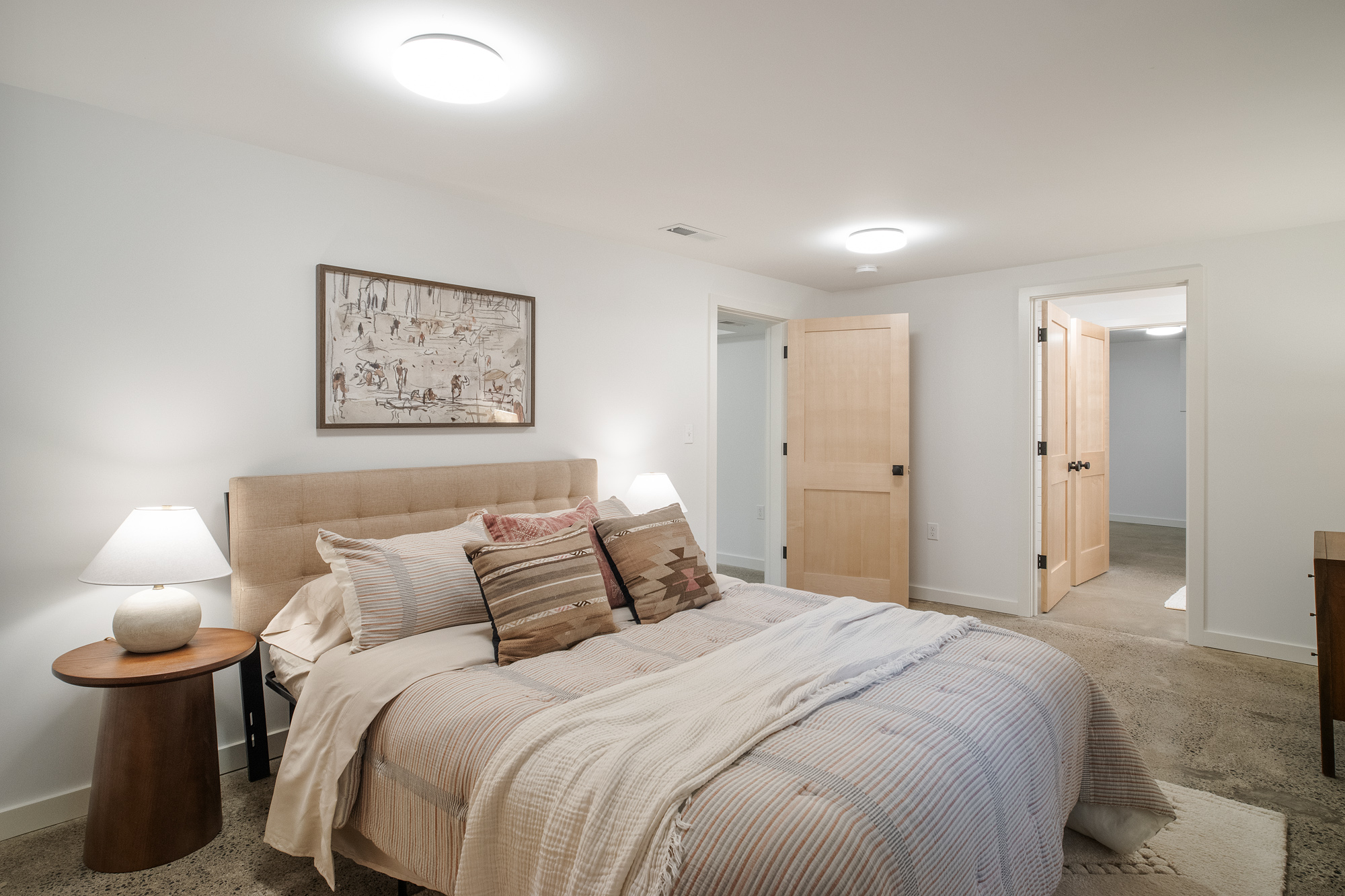 Finished basement guest bedroom with carpet, maple doors, and view into the hall beyond, NE 9th Remodel by Tweto Architecture