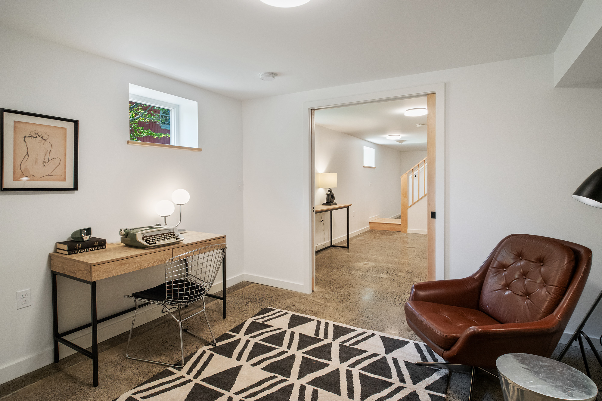 Finished basement office with polished concrete floor, high hopper window, and view through the open doorway to the stair hall, NE 9th Remodel by Tweto Architecture