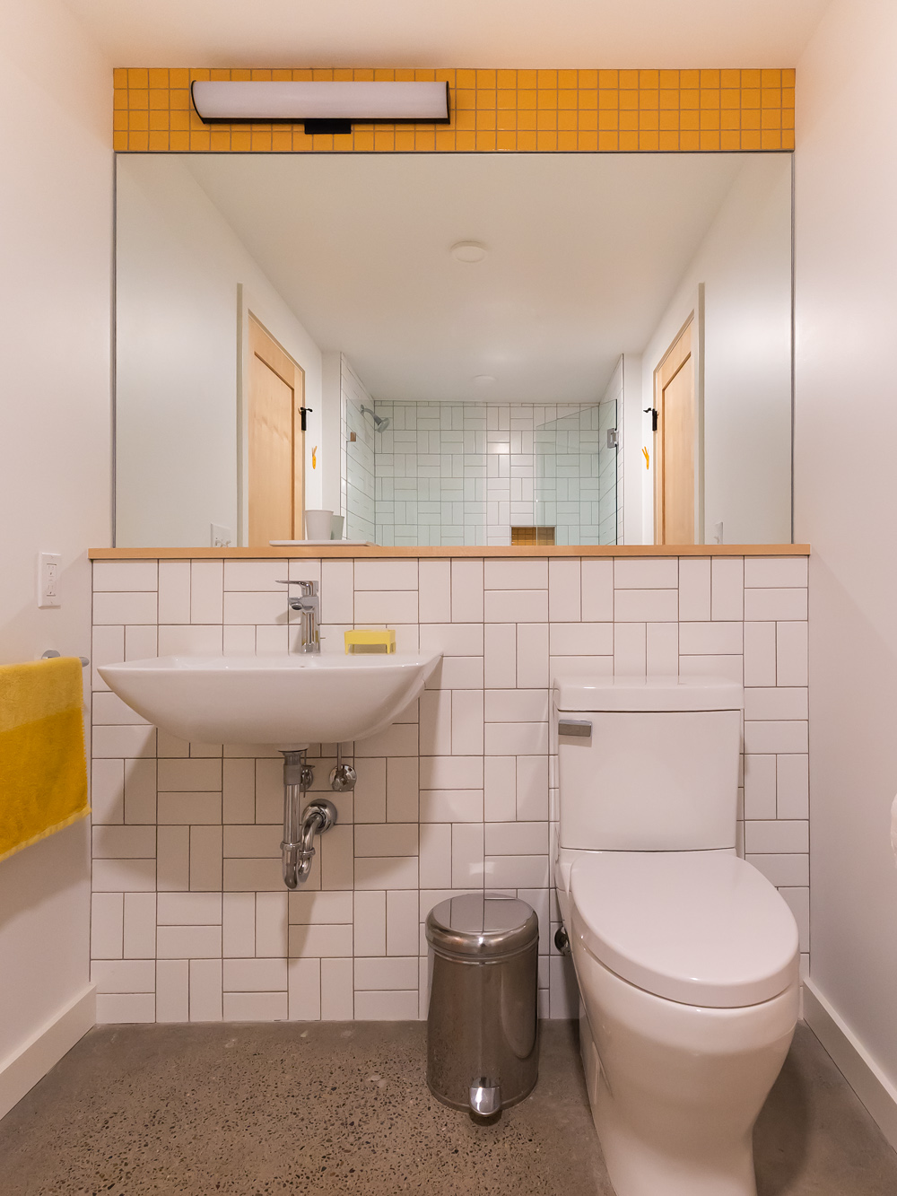 Basement bathroom vanity with wall-mount sink, white subway tile in a running bond pattern, and amber tile accent at the top, NE 9th Remodel by Tweto Architecture