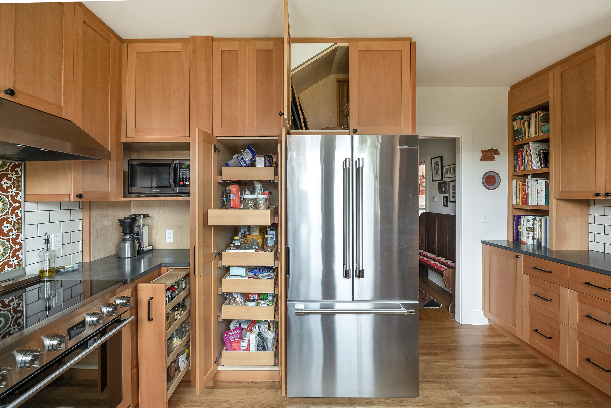 Pantry cabinet open showing pull-out shelves and integrated refrigerator alongside the range and cookbook shelves, Sabin Kitchen by Tweto Architecture