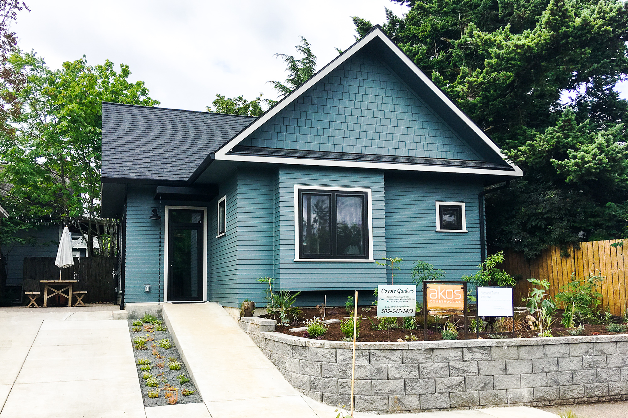 Front exterior of the recording studio with blue-green lap siding, gable roof, and new plantings along a stone retaining wall, Siskiyou Street Recording Studio by Tweto Architecture