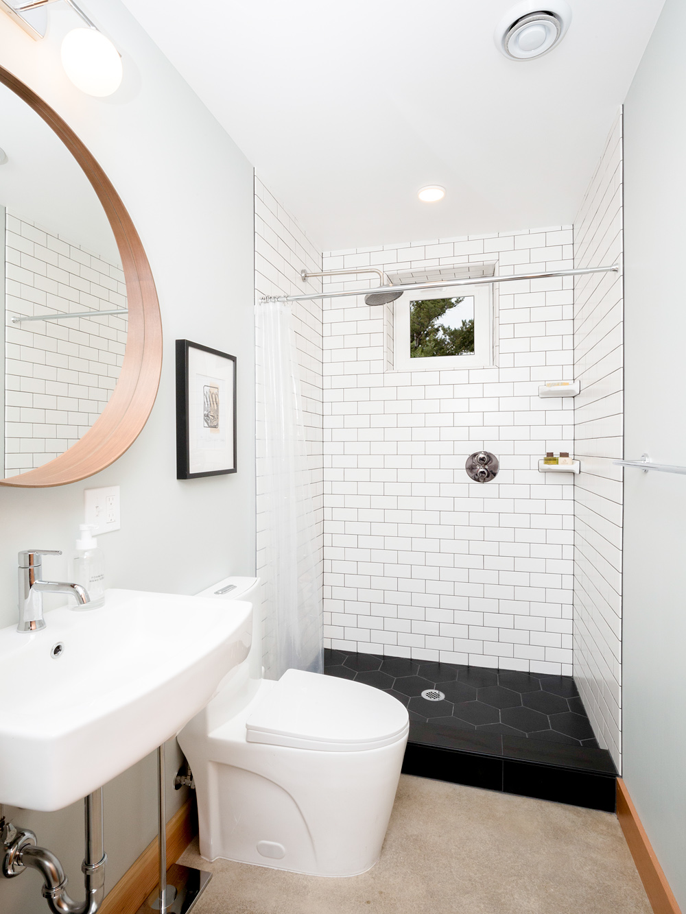 Bathroom with white subway tile walls, black hexagonal tile shower floor, round wood-framed mirror, and pedestal sink, Siskiyou Street Recording Studio by Tweto Architecture